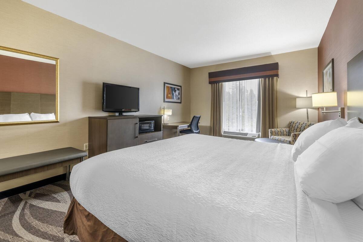 A hotel room with a large bed, a desk with a computer, a television, and a window with curtains.
