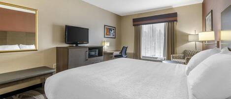 Habitación de hotel con una cama grande, un escritorio con computadora, televisión y ventana con cortinas.