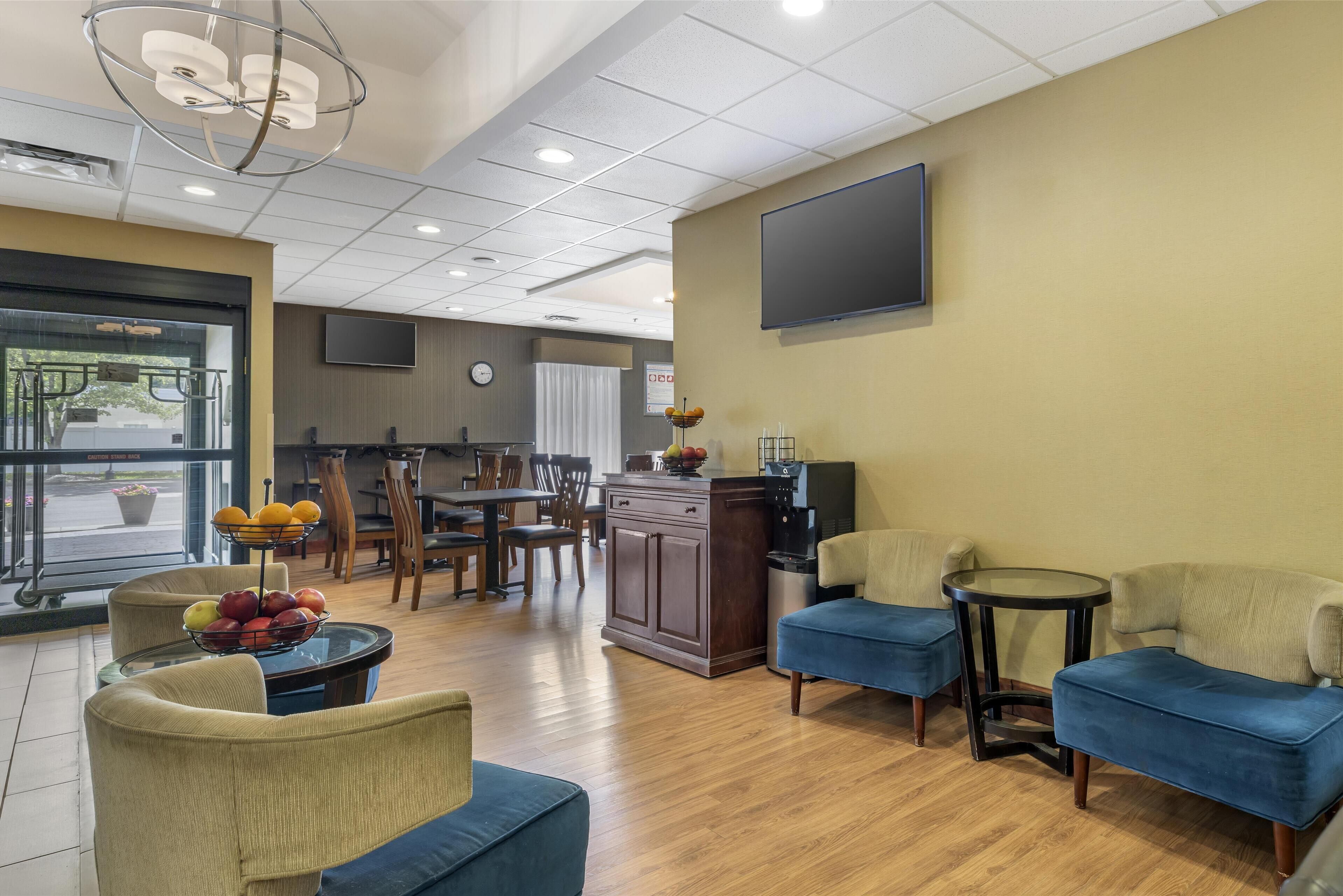 A hotel lobby with seating areas, a coffee station, and a television mounted on the wall.