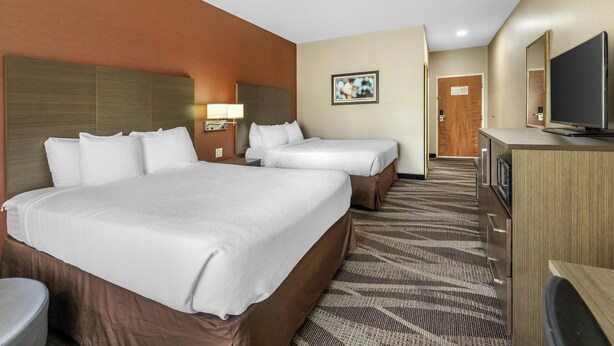 A hotel room with two beds, a television, a desk, and a bathroom.