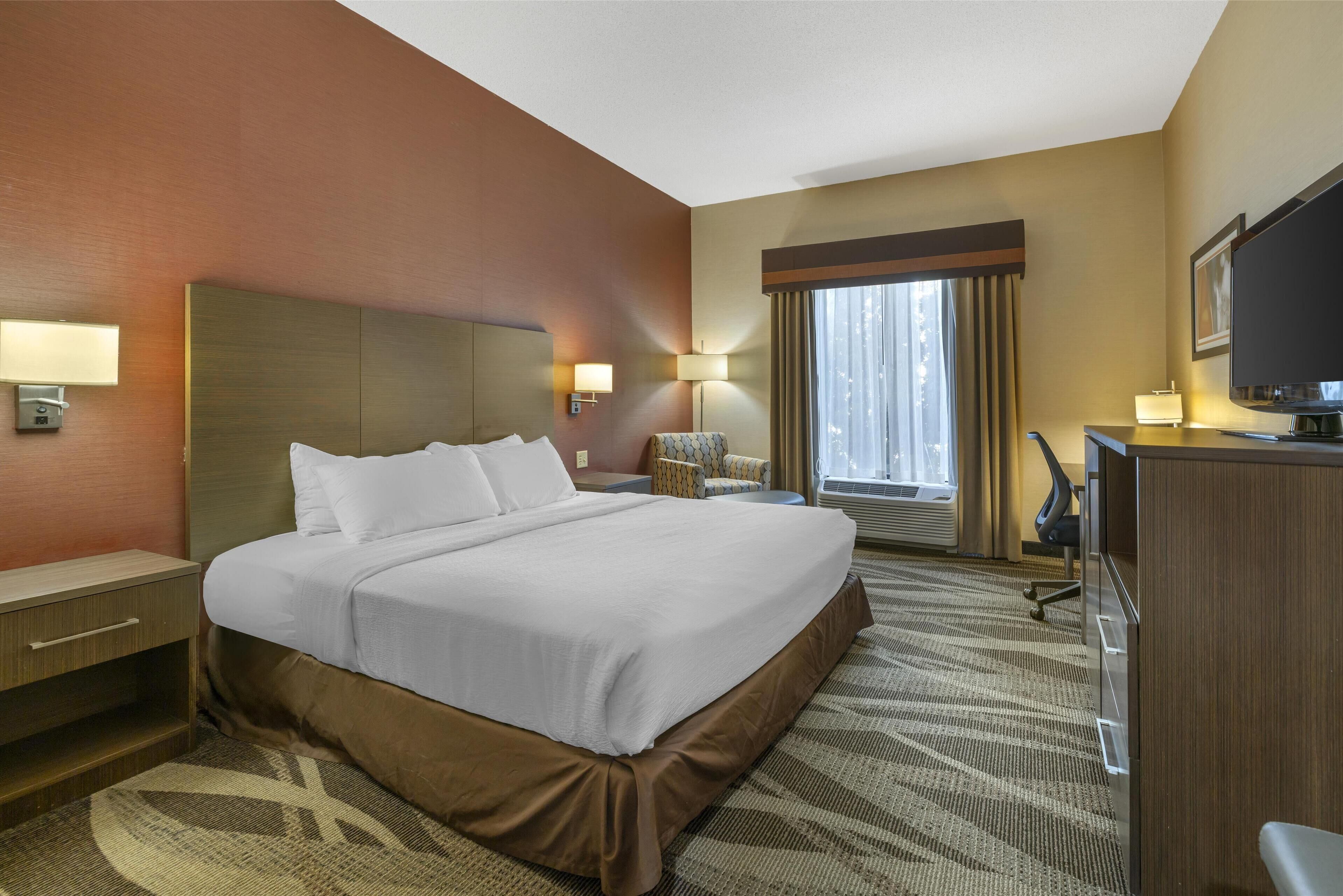 A hotel room with a large bed, bedside lamps, a desk, a chair, and a television.
