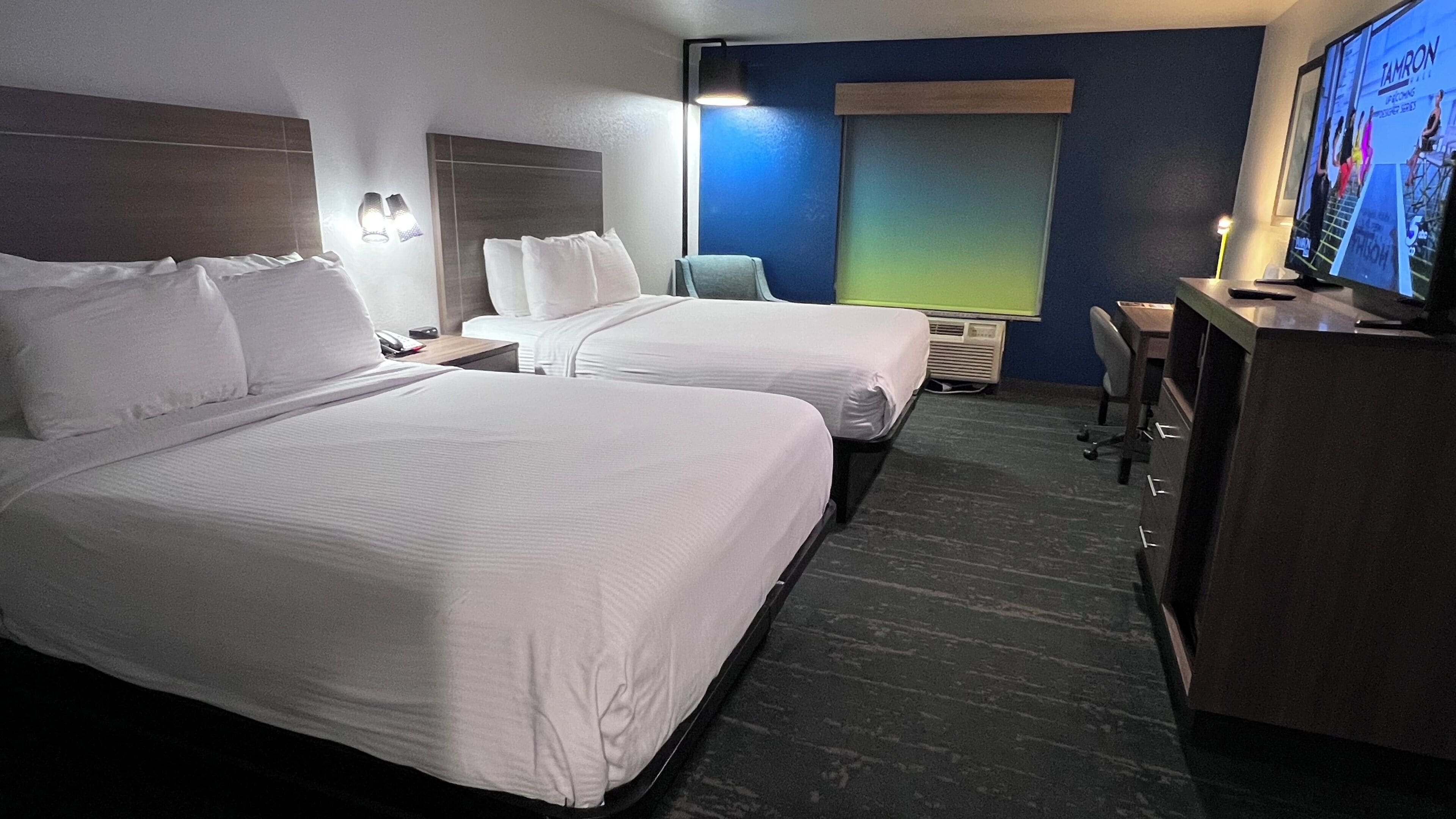 Une chambre d’hôtel avec deux lits, un bureau, une chaise, une télévision et une fenêtre.