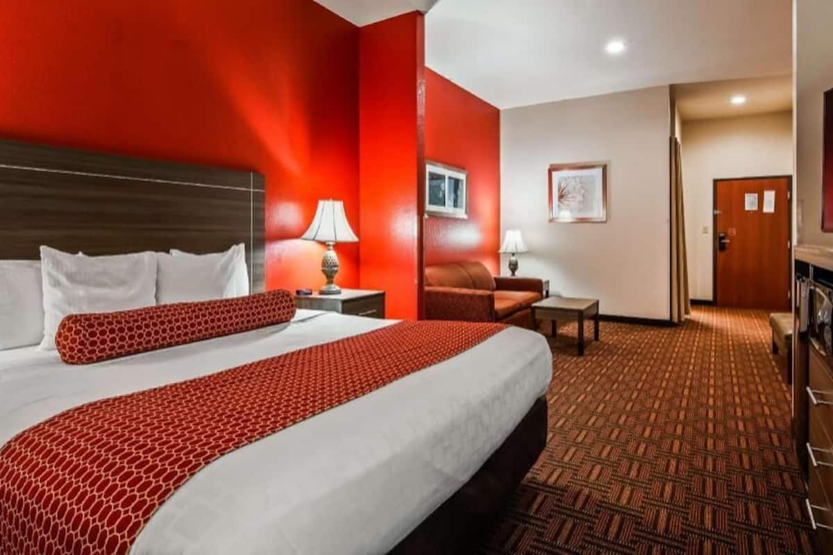 A hotel room with a large bed, a desk, a chair, a TV, and a door leading to a hallway.