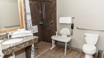 A bathroom with a granite countertop sink, a white toilet, a shower with a glass door, and a towel rack.