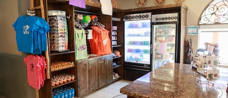 Interior de una tienda con estantes llenos de aperitivos, un refrigerador y una barra con diversos artículos.