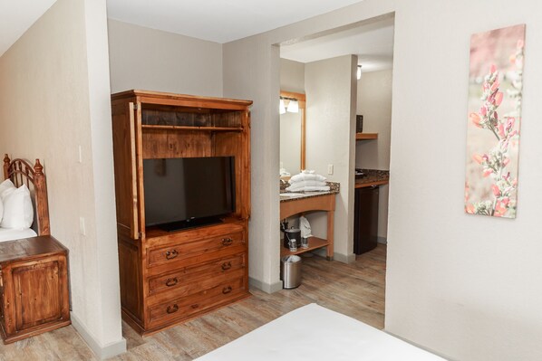 A bedroom with a wooden dresser, a television, a bed, and a bathroom visible through an open door.