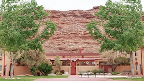 A building with a red exterior, a central staircase, and a surrounding garden with benches and trees. - Aarchway Inn (Moab)