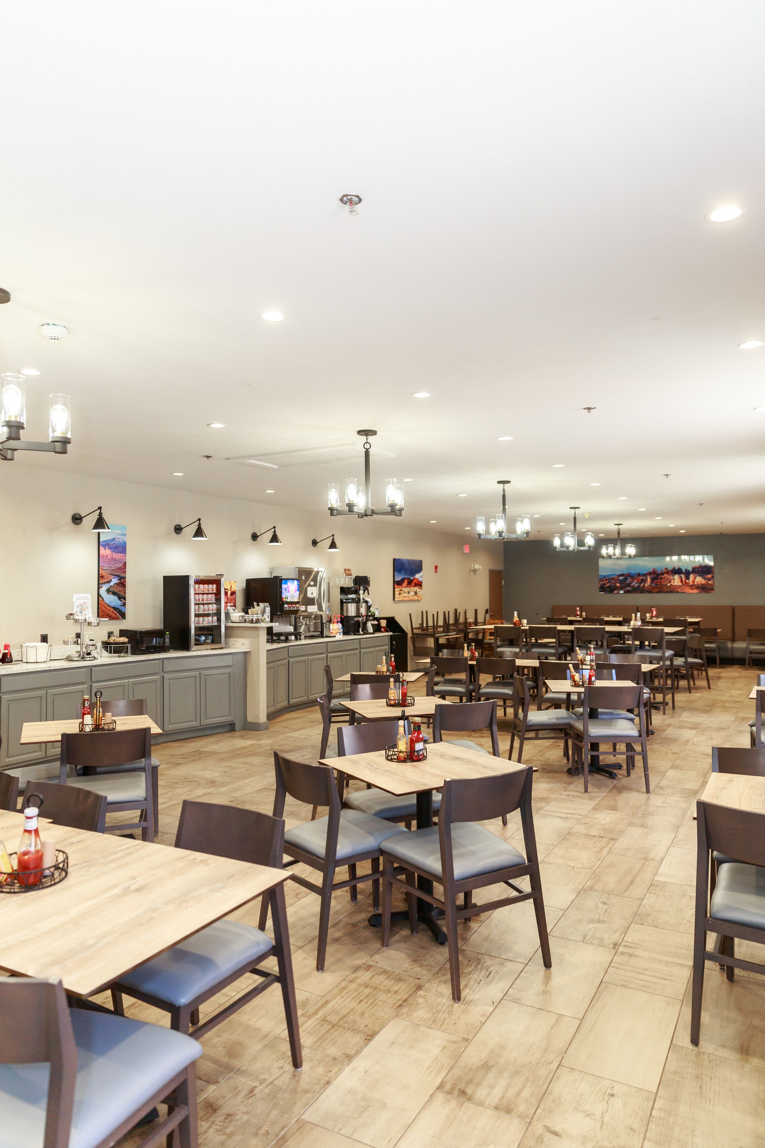 A spacious restaurant with multiple tables and chairs, a counter with a coffee machine, and artwork on the walls.