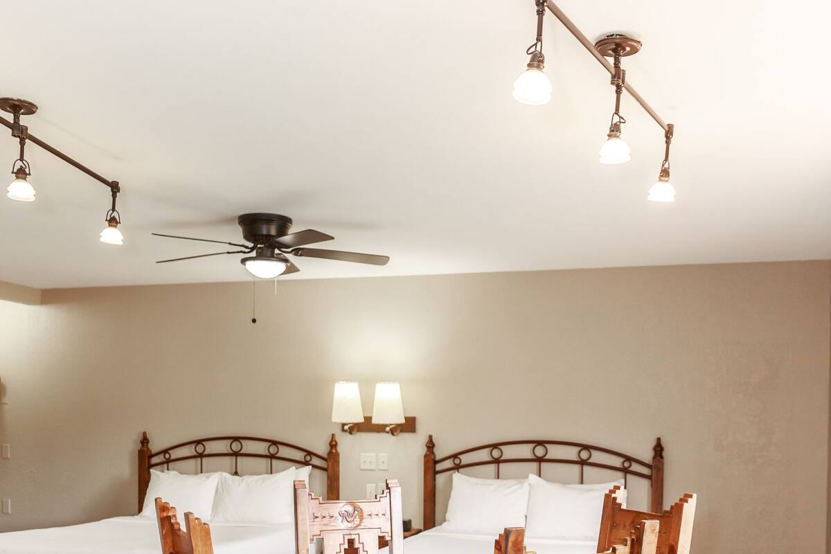 A hotel room with a bed, a dining table with chairs, a ceiling fan, and a chandelier.