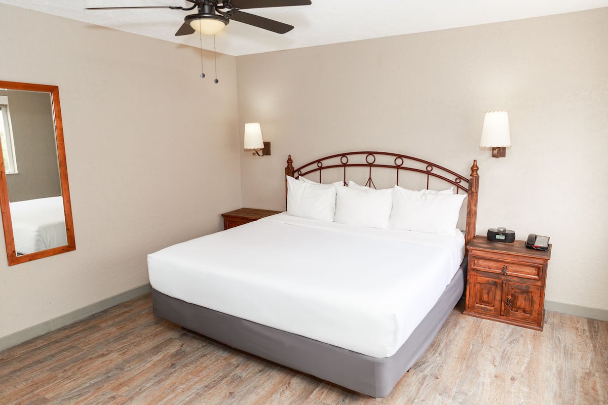 A neatly made bed with a wooden headboard, two bedside tables with lamps, a ceiling fan, and a mirror on the wall.