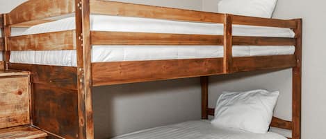 Un lit superposé avec une structure en bois et une literie blanche, dans une pièce dotée d’un plancher en bois et de murs blancs.