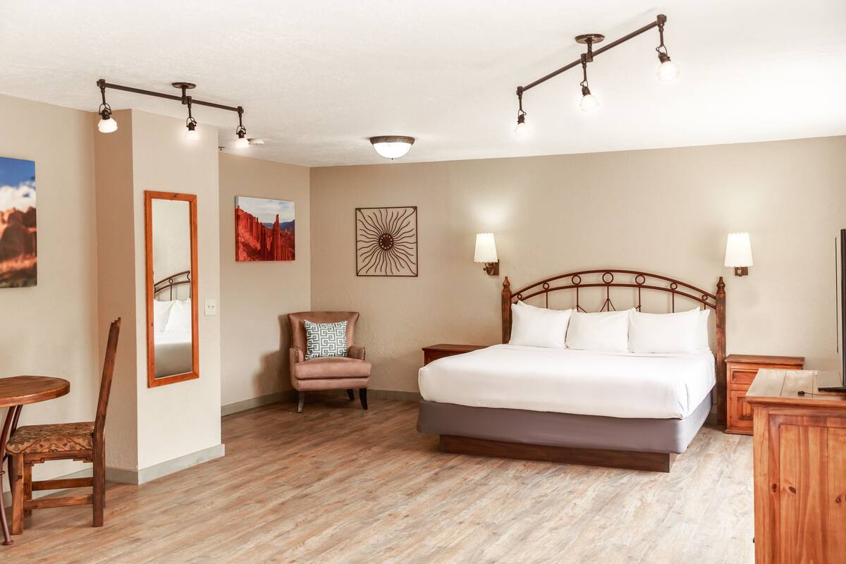 A bedroom with a large bed, a chair, a small table, and a mirror.