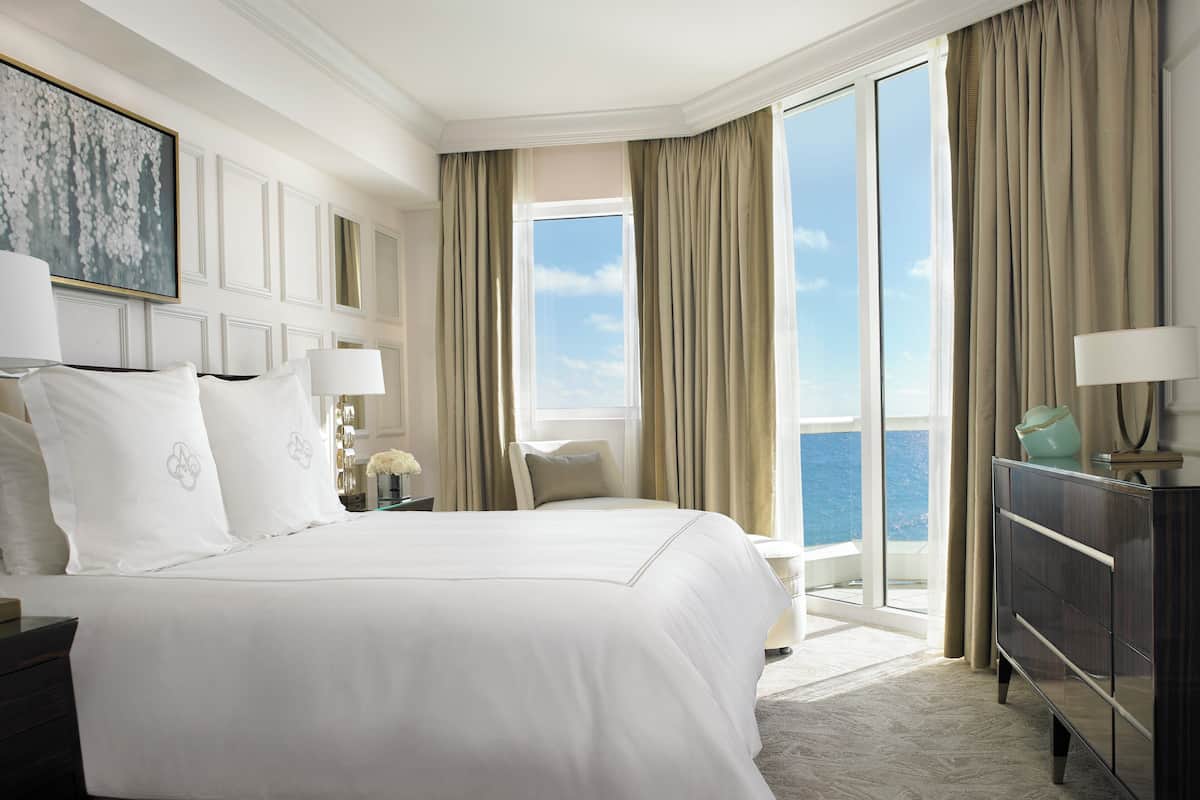 Habitación de hotel con una cama grande, una mesita de noche, un aparador y vista al mar.