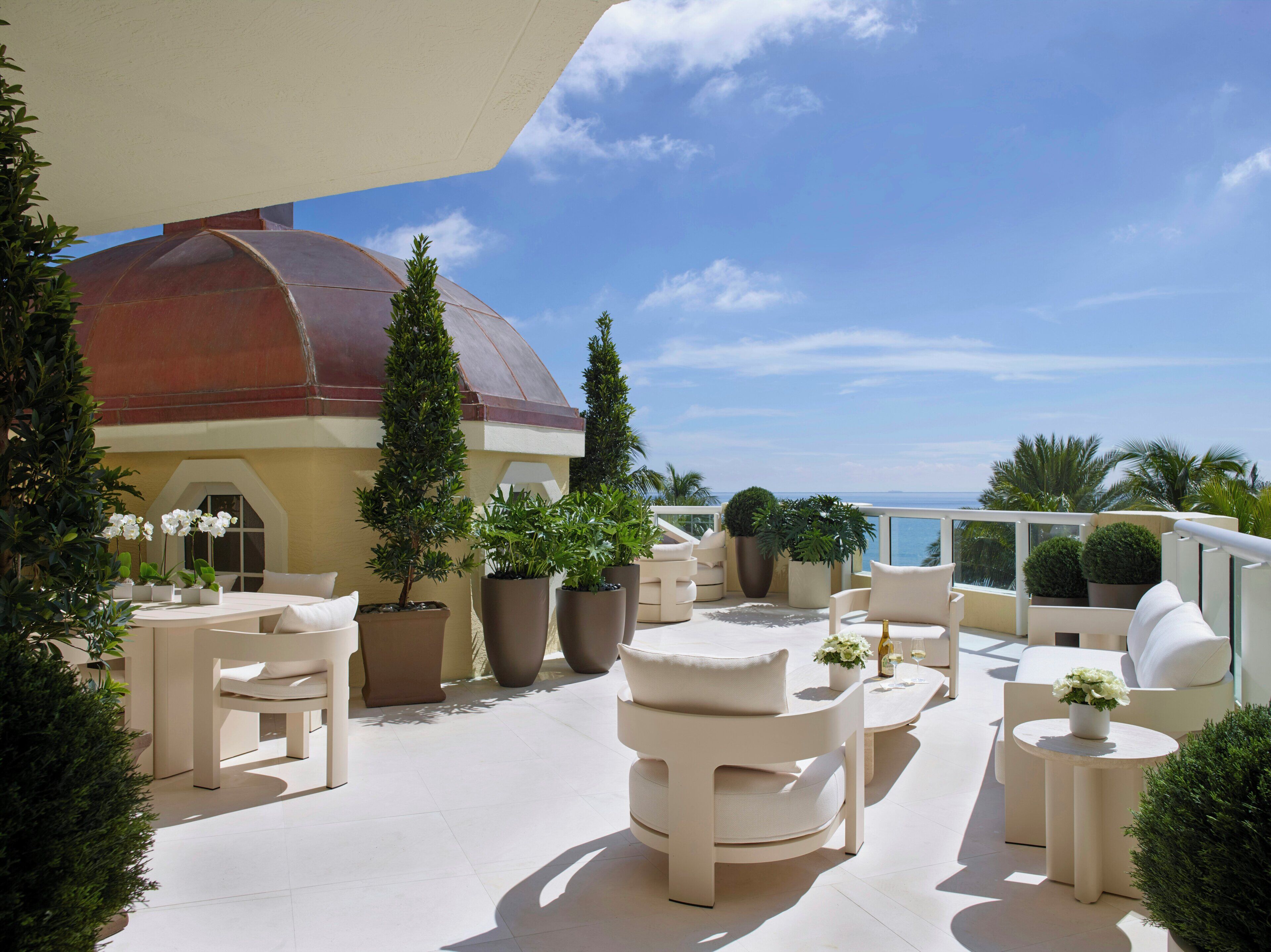 Una terraza en la azotea con mobiliario exterior, plantas en macetas y vistas al mar.