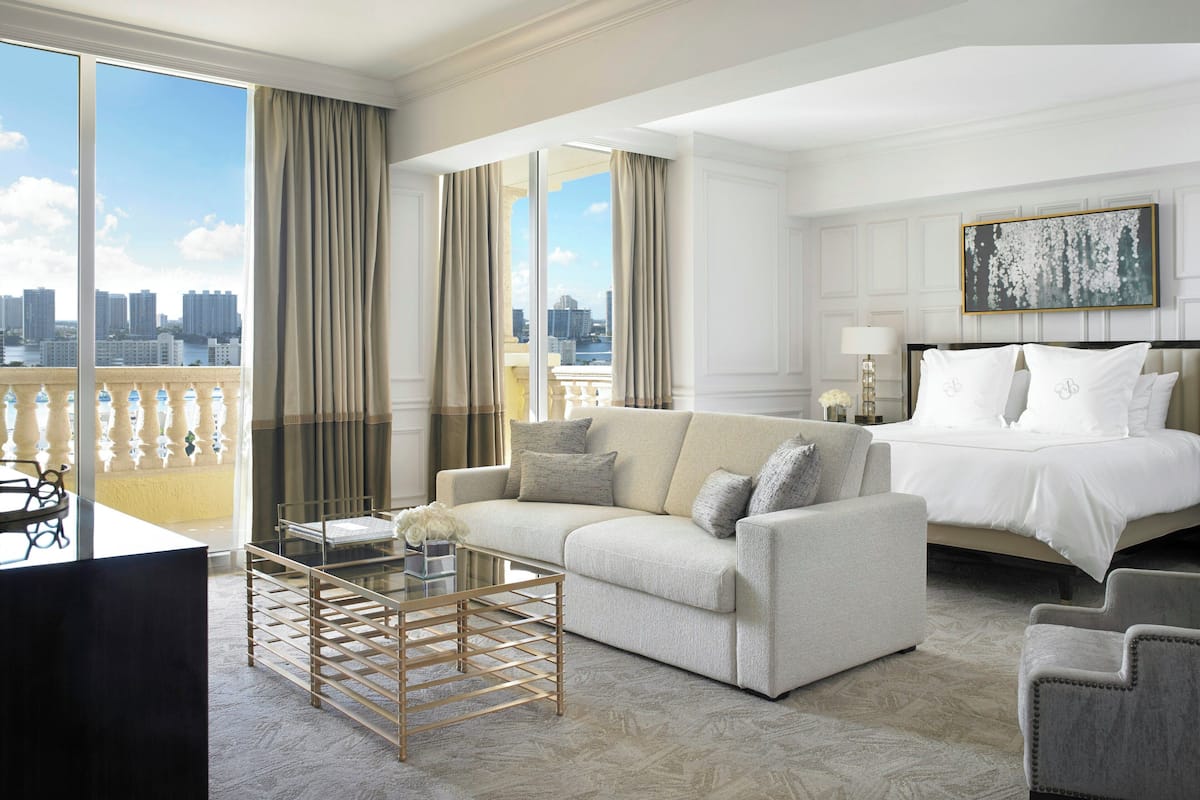 A hotel room with a large window, a sofa, a bed, and a small table.