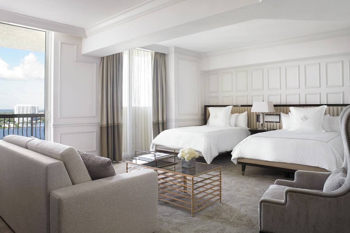 A hotel room with two beds, a sofa, a coffee table, and a view of the city.