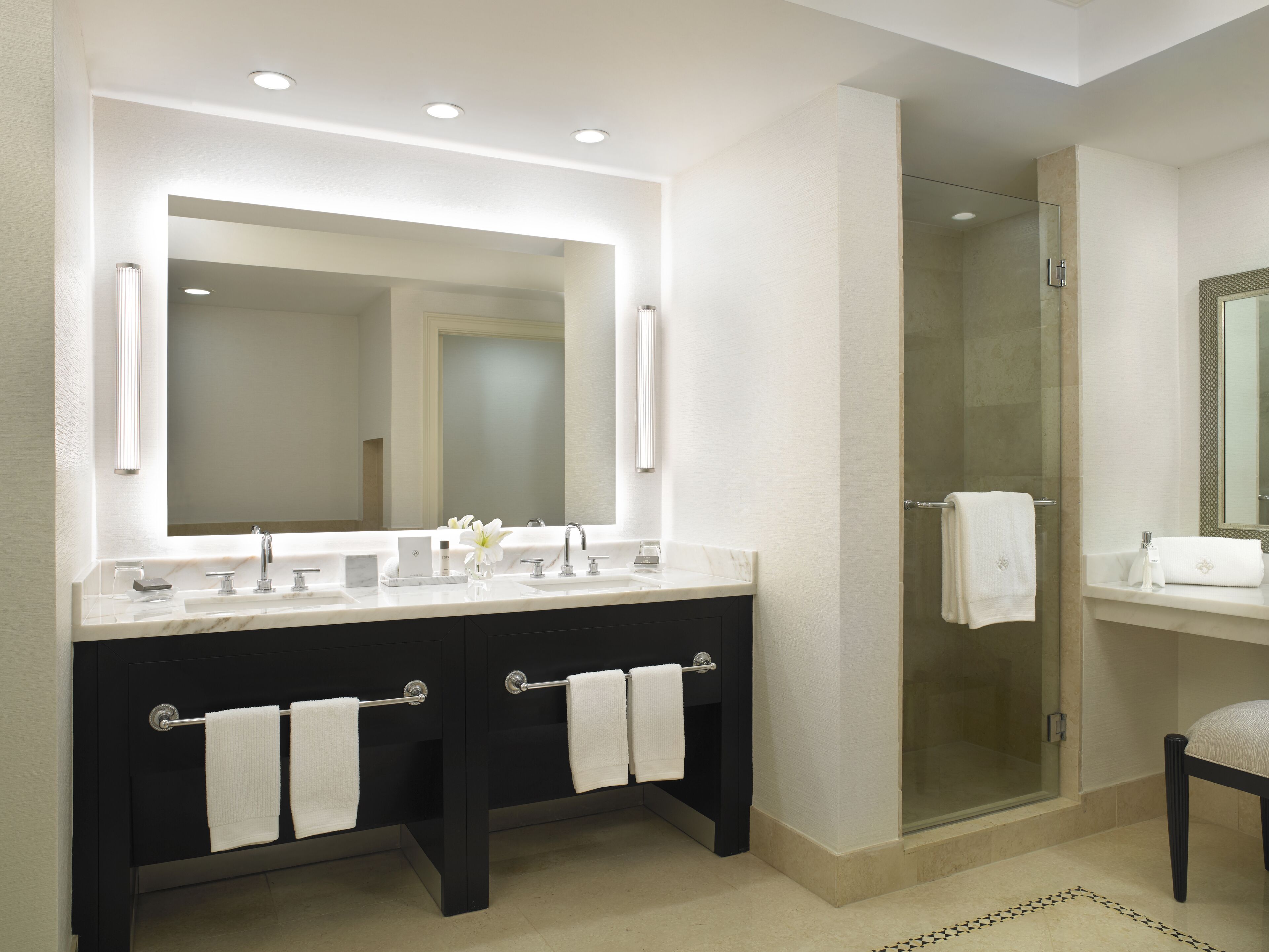 A modern bathroom with a large mirror, dual sinks, and a glass shower enclosure.