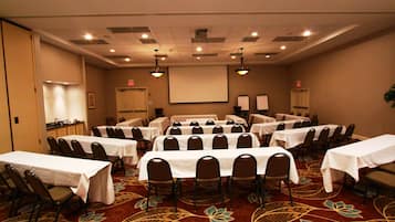 A conference room with multiple tables and chairs, a projector screen, and a carpeted floor.