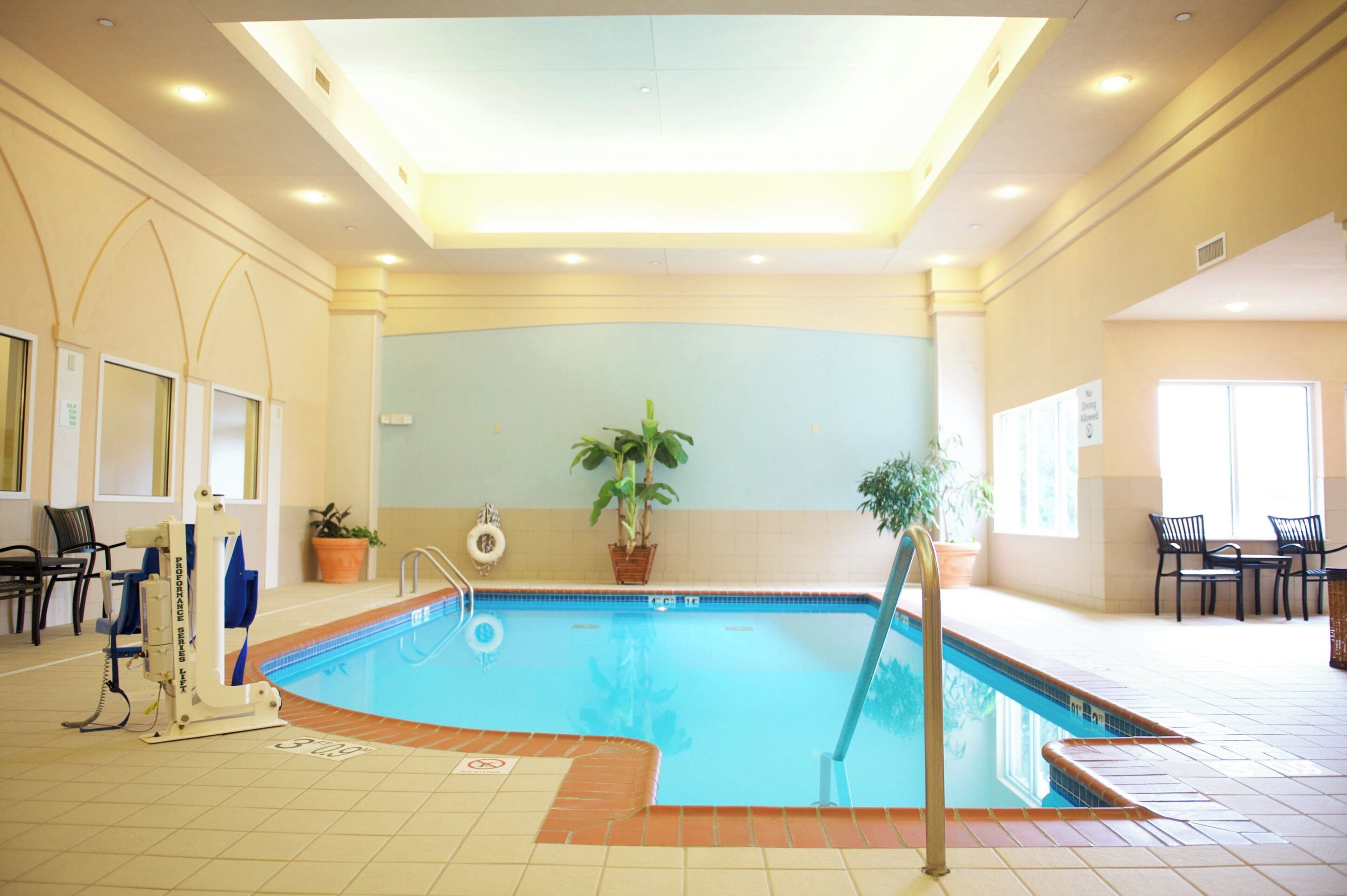 An indoor swimming pool with a tiled floor, a lifeguard stand, and potted plants.