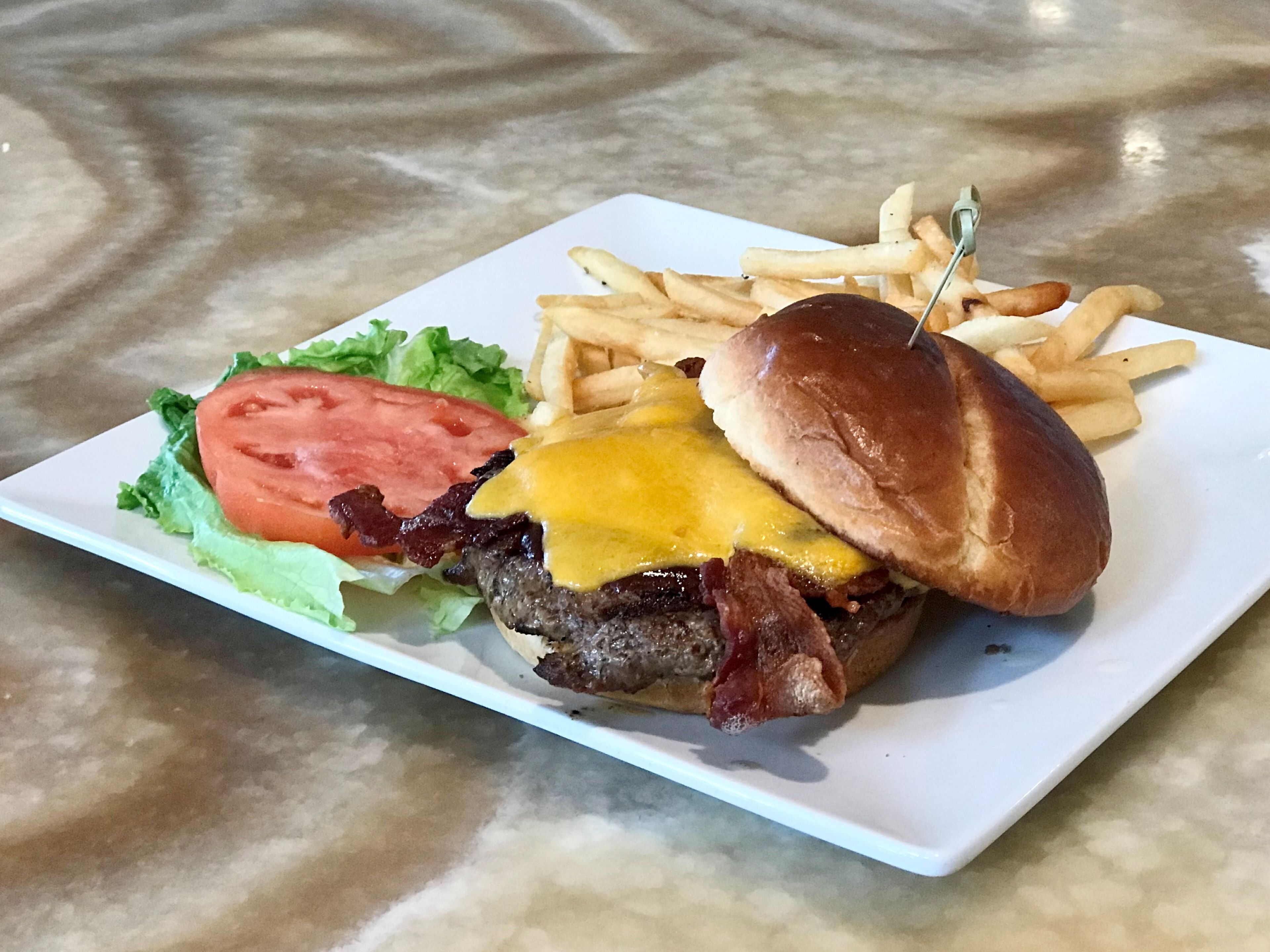 Une assiette avec un hamburger, des frites et une tranche de tomate.
