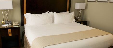 A hotel room with a large bed, two bedside tables with lamps, a headboard, and framed artwork on the wall.