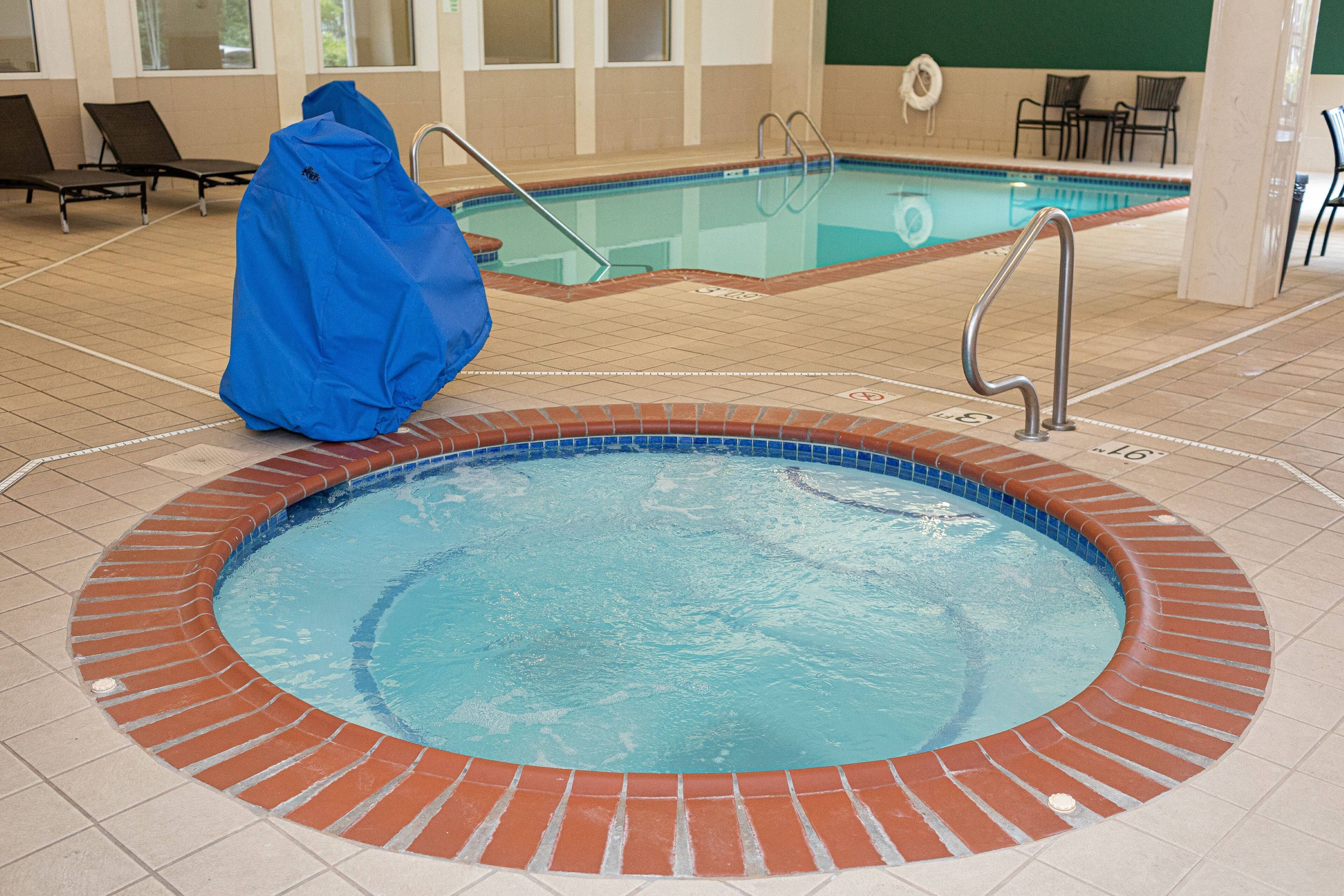Una piscina interior con borde de ladrillo, una silla de salvavidas y sillas de descanso.