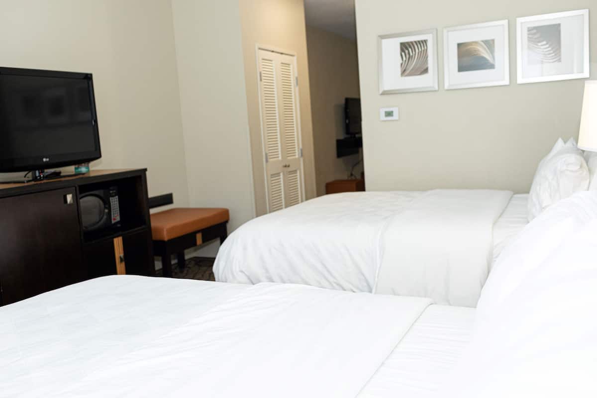 Habitación de hotel con dos camas, televisión, escritorio con silla y cuadros en la pared.
