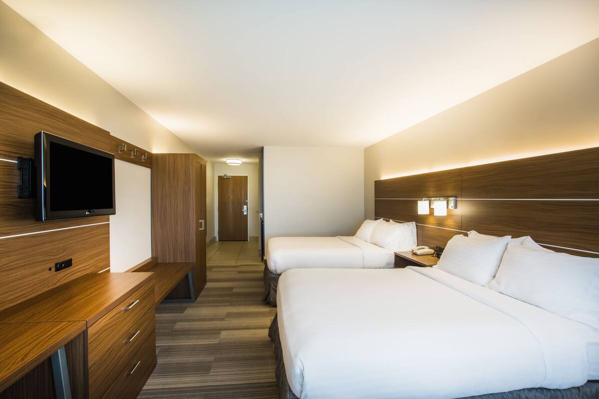 A hotel room with a TV, two beds, a desk, and a bathroom visible in the background.