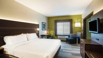 A hotel room with a large bed, a desk, a chair, a television, and a window.