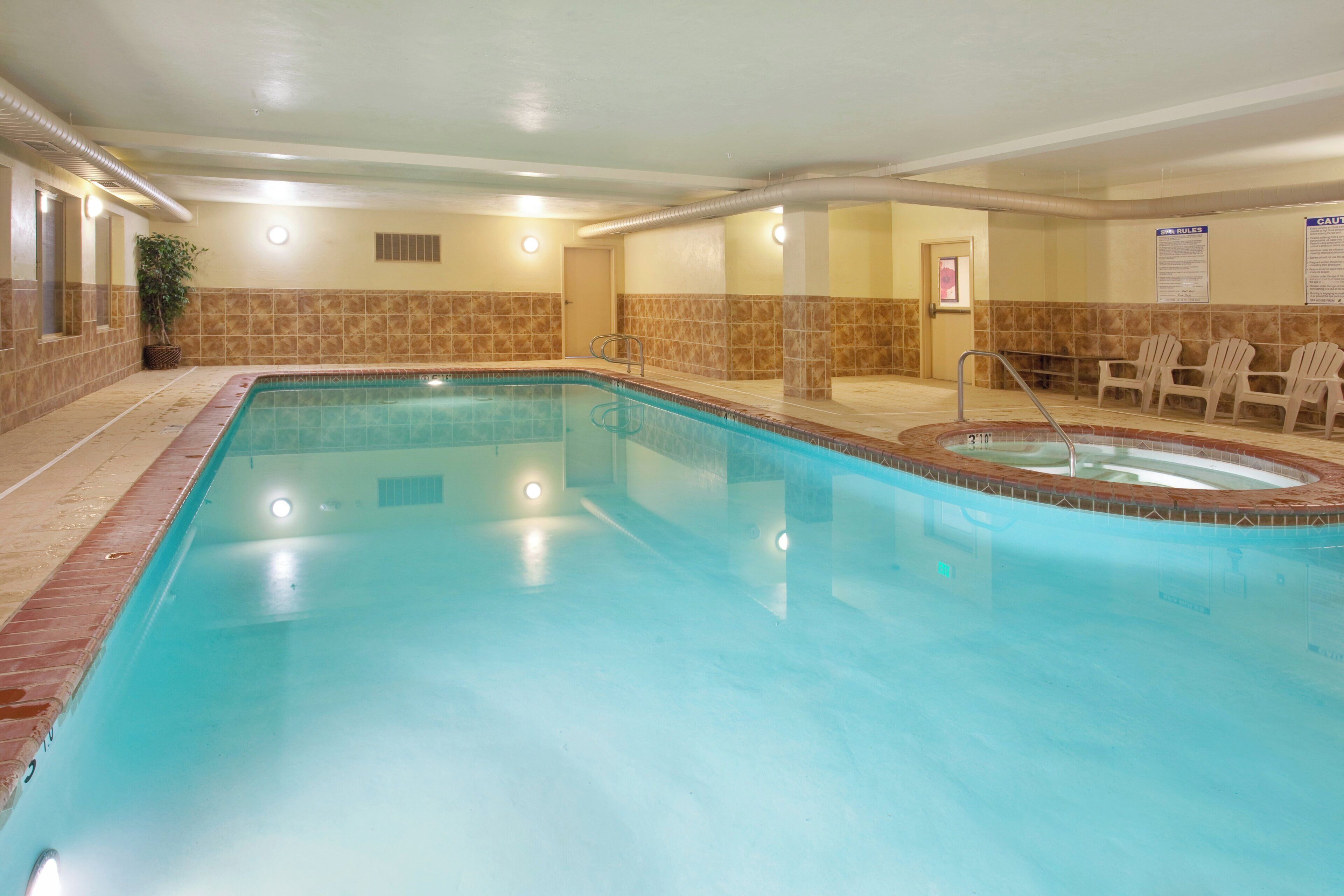 A swimming pool with a hot tub, tiled walls, and a door leading to another room.