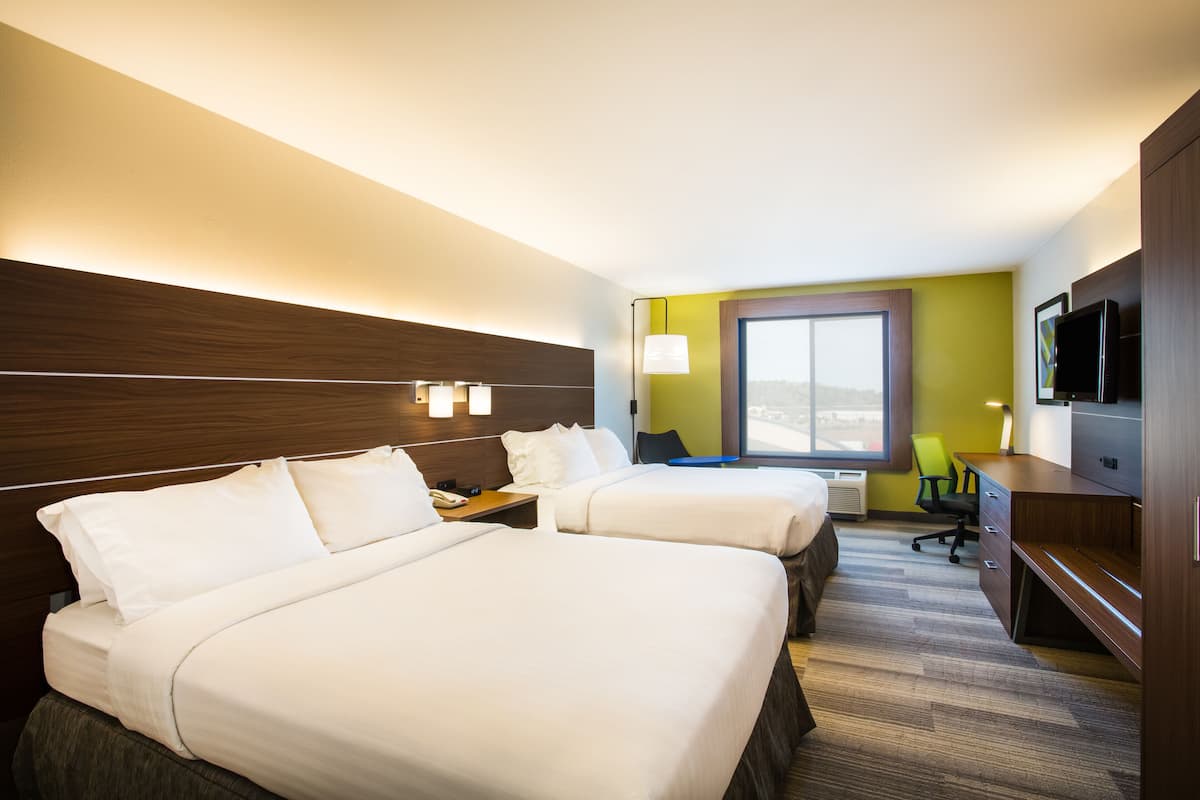 A hotel room with two beds, a desk, a chair, a TV, and a window with a view.