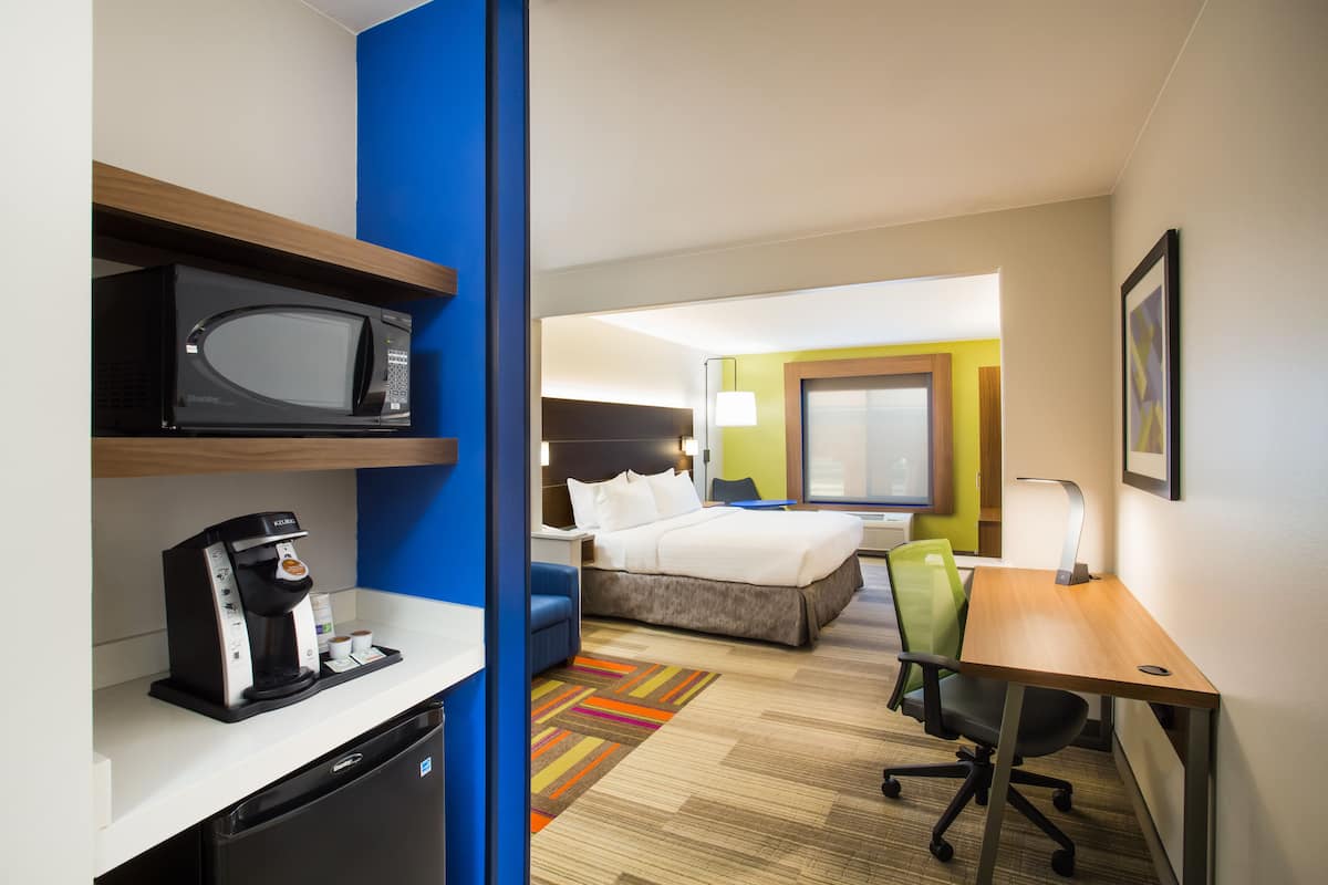 A hotel room with a bed, a desk, a microwave, a coffee maker, and a chair.