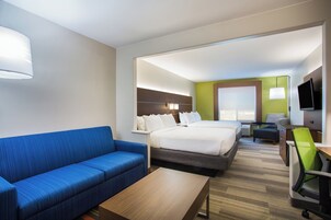 Habitación de hotel con sofá azul, cama con ropa blanca, escritorio con silla y televisor.