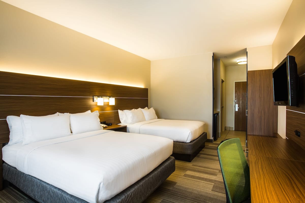 A hotel room with two beds, a desk, a chair, a TV, and a hallway.