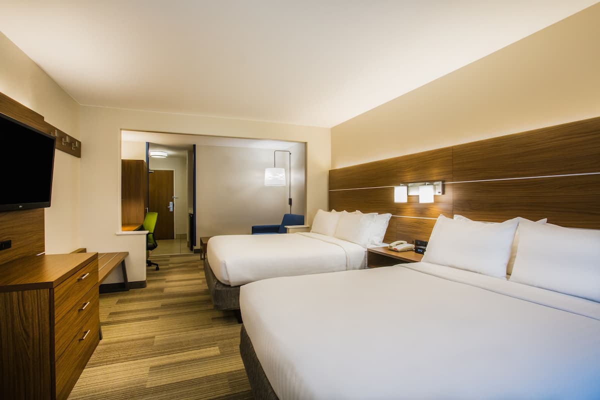 A hotel room with two beds, a desk, a chair, a TV, and a mirror.