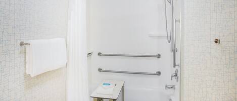 A bathroom with a white bathtub, a shower, and a handrail.