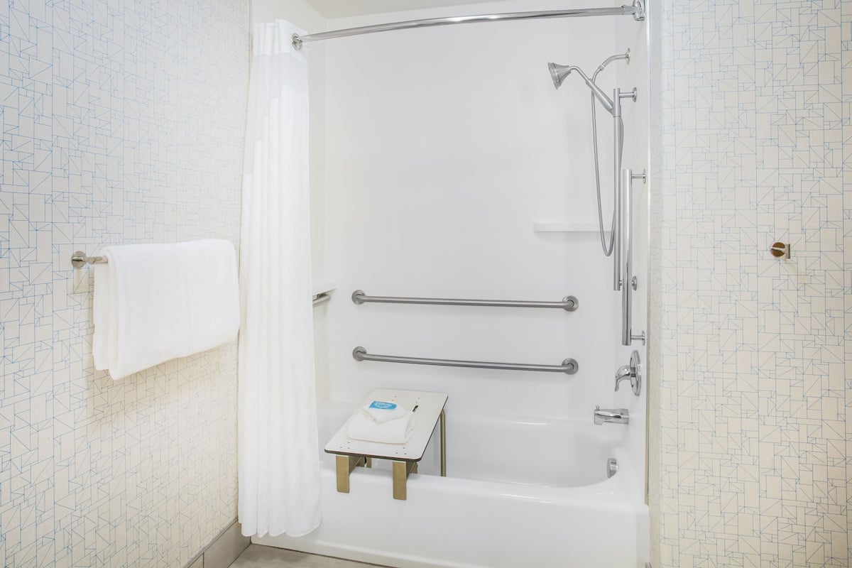 A modern bathroom with a bathtub, grab bars, and a small table with a towel.
