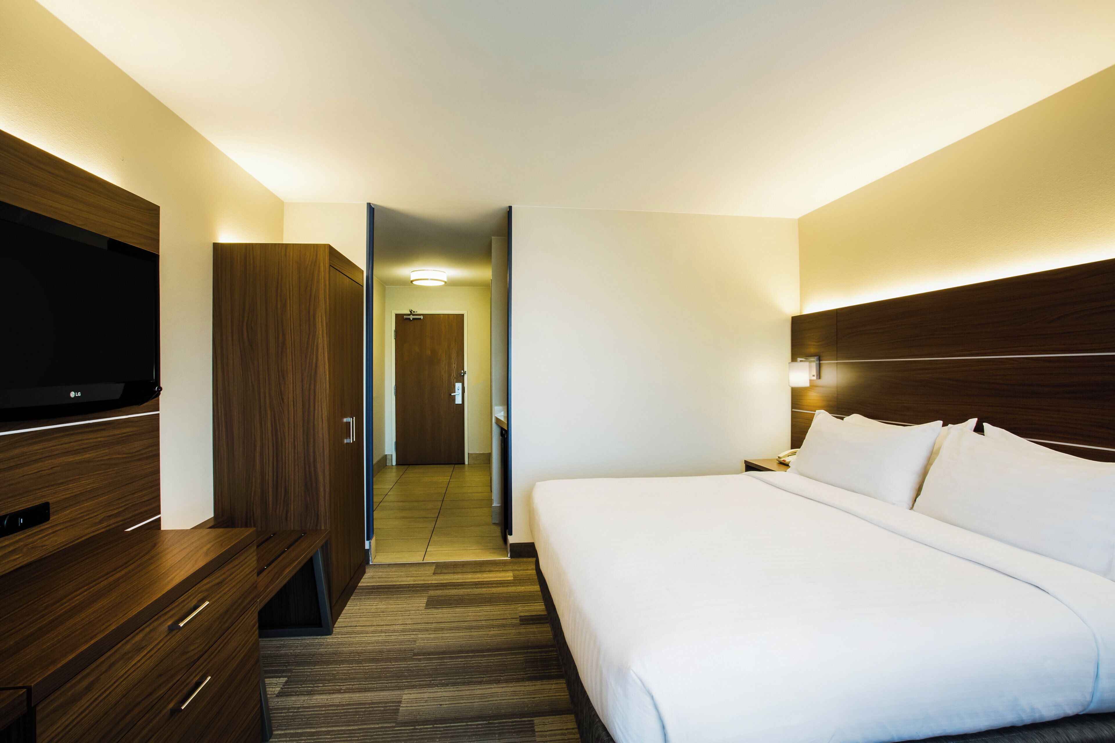 A hotel room with a bed, a TV, a wardrobe, and a door leading to a hallway.