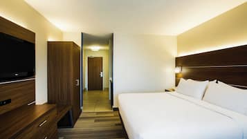A hotel room with a bed, a TV, a wardrobe, and a door leading to a hallway.