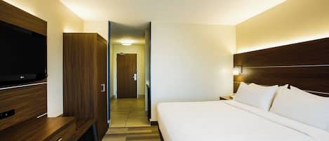 A hotel room with a bed, a TV, a wardrobe, and a door leading to a hallway.