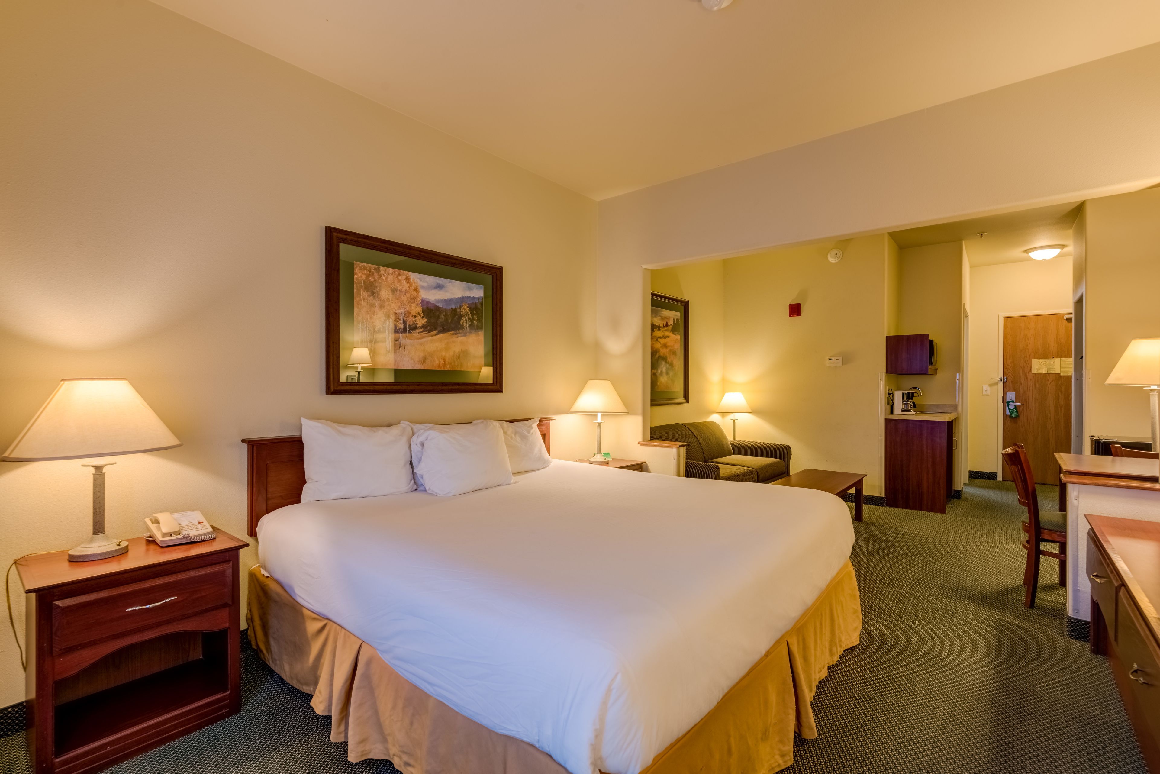 A hotel room with a large bed, two bedside lamps, a desk, a chair, and a painting on the wall.