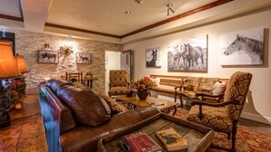 Una sala de estar acogedora con una pared de piedra decorativa, sofá de cuero, sillones estampados y arte temático de caballos.