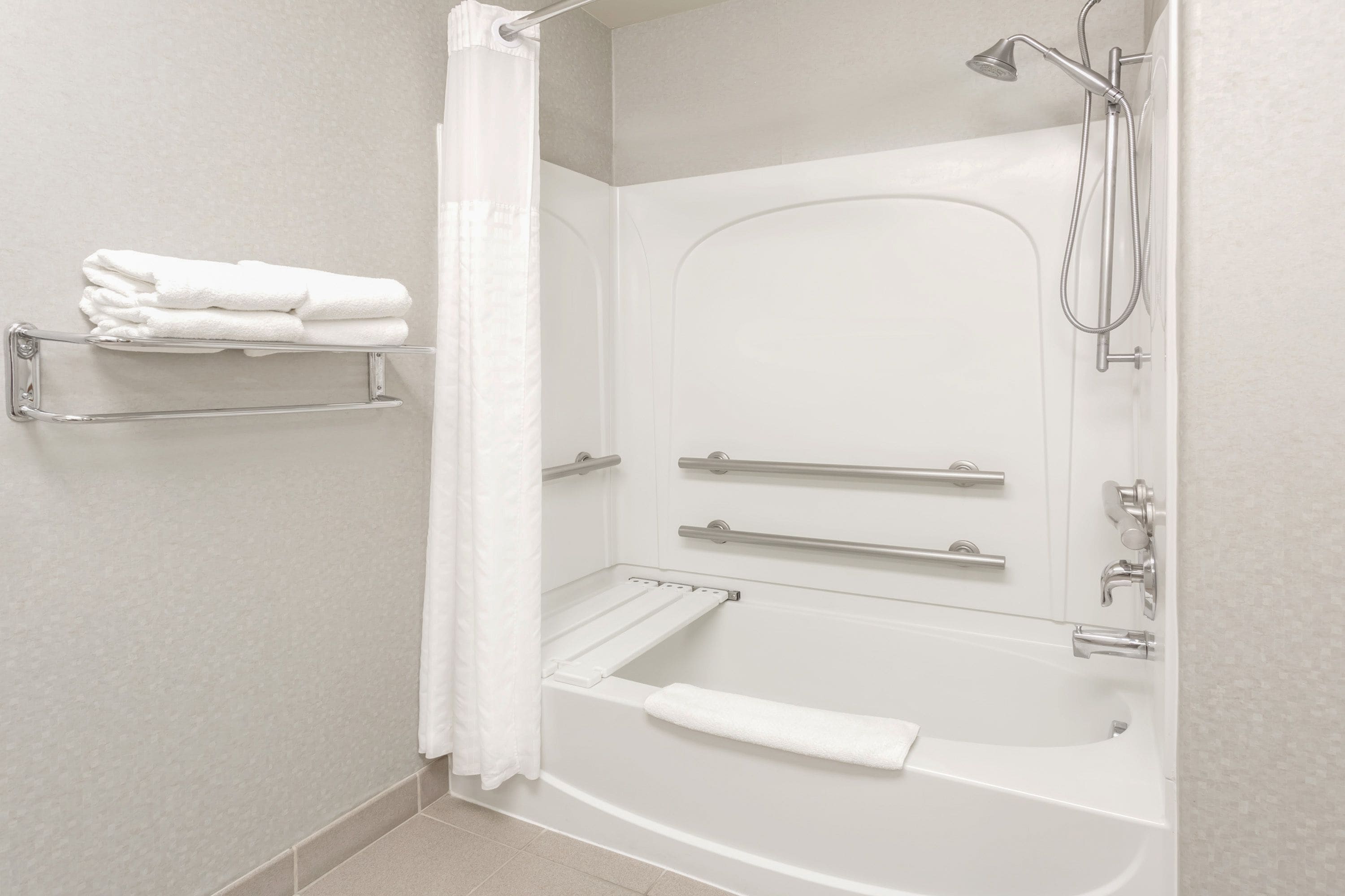 A modern bathroom with a bathtub, shower, and handrails.