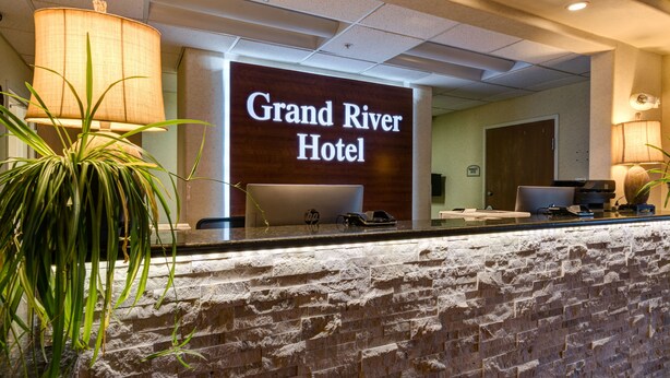Un mostrador de recepción en el Grand River Hotel con un fondo de pared de piedra y un letrero iluminado grande.
