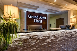 Un mostrador de recepción en el Grand River Hotel con un fondo de pared de piedra y un letrero iluminado grande.