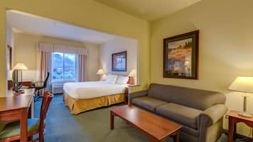 A hotel room with a bed, a sofa, a desk, and a chair. There are two lamps on either side of the bed and a painting on the wall.