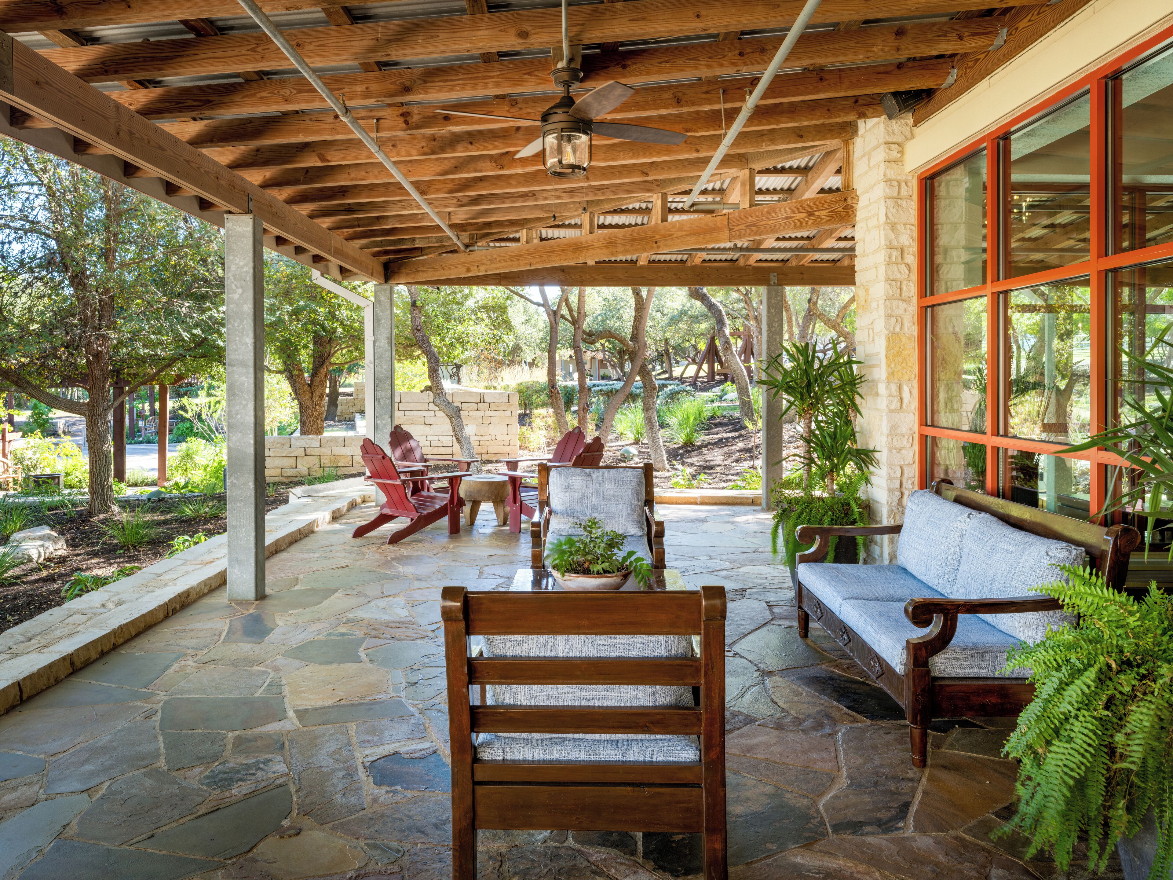 Un patio exterior con suelo de piedra, mobiliario de madera y vistas a un jardín.