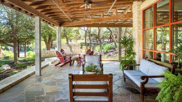 Un patio exterior con suelo de piedra, mobiliario de madera y vistas a un jardín.