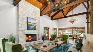 A spacious living room with a fireplace, green armchairs, a sofa with patterned cushions, and a large window offering a view of the outdoors. - Hyatt Vacation Club at Wild Oak Ranch, San Antonio (San Antonio)