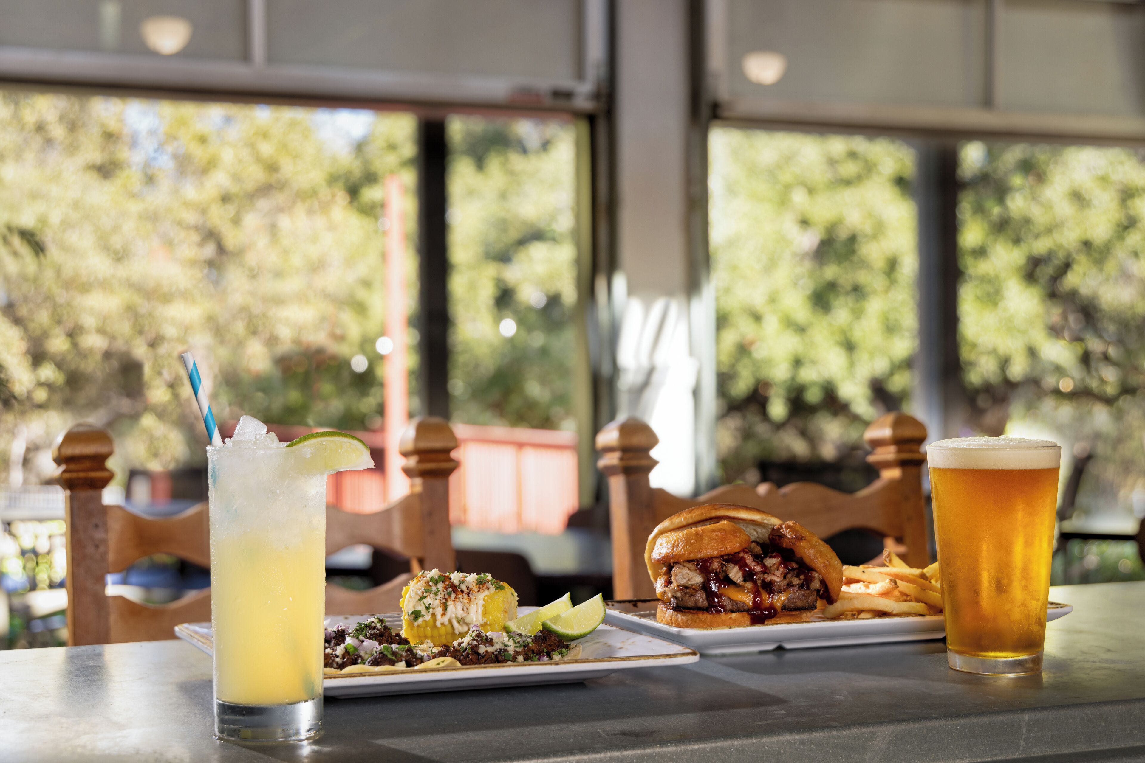 Eine Mahlzeit mit einem Burger und Pommes, ein Glas Bier und ein Cocktail mit Limettenspalte auf einem Tisch.